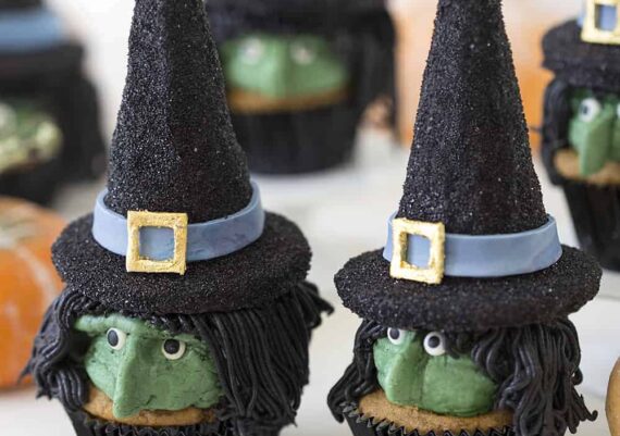 Two Halloween witch hat cupcakes with more cupcakes in the background.
