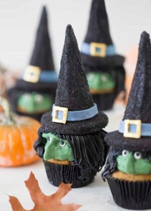 A photo of realistic looking witch cupcakes on a white table.