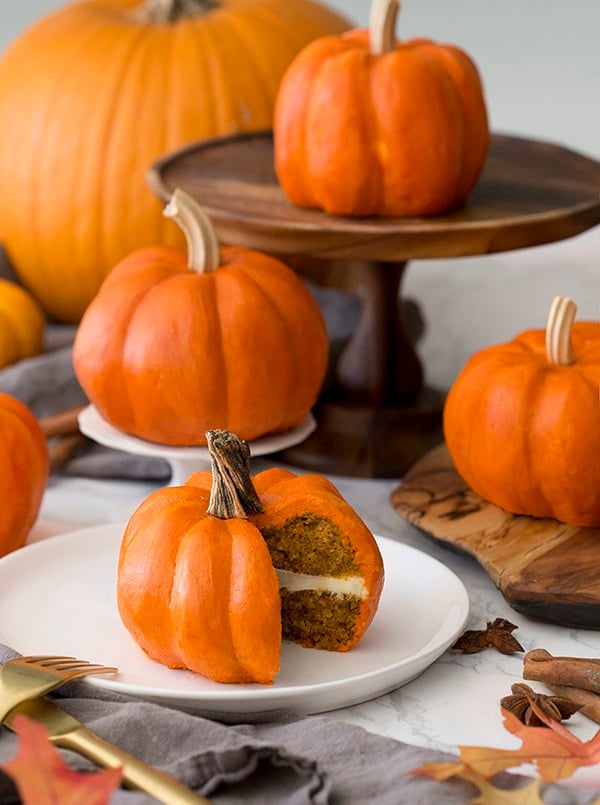 mini pumpkin cakes on a table with real pumpkins mixed in.