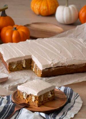 A pumpkin poke cake covered in brown butter frosting with a pice in the foreground.