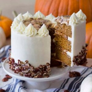 A slice of pumpkin pecan cake being lifted from the rest of the cake from a white cake stand.