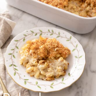 Baked mac and cheese with toasted breadcrumbs on a plate in front of a baking dish.
