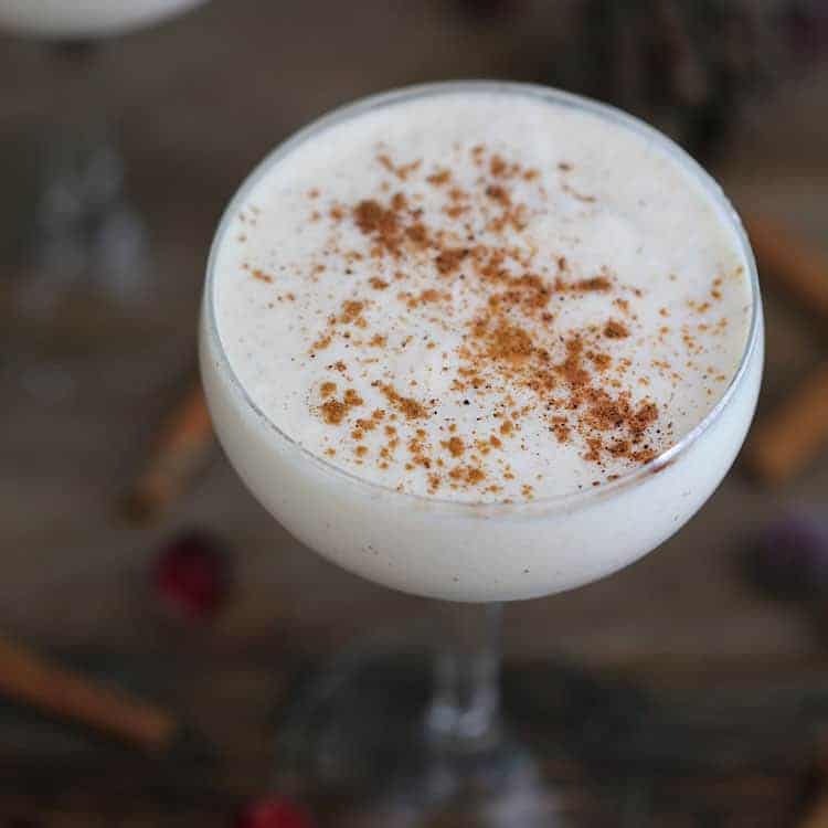 a coupe glass filled with eggnog on a wooden table