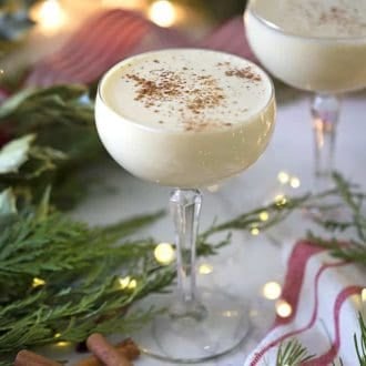 eggnog in a coupe glass next to Christmas lights and greens
