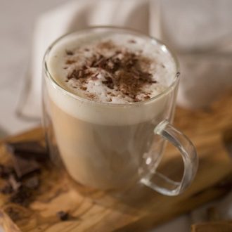 A photo of a latte with cinnamon and chocolate in a glass mug.