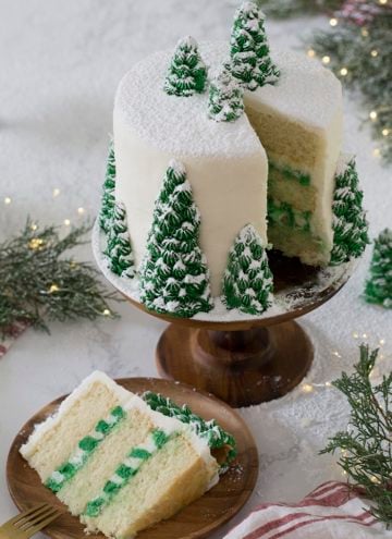 A photo of a christmas tree cake covered in buttercream pine trees and dusted with powdered sugar