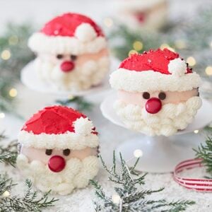 A photo showing a group of Santa cupcakes on a white marble table with greenery.