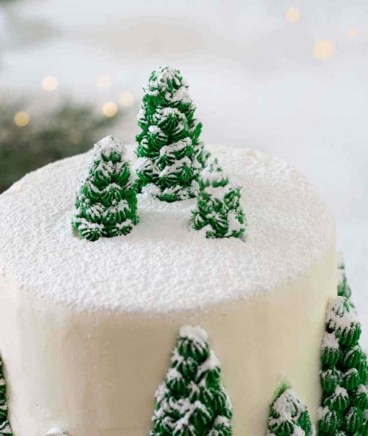 A close up photo of a Christmas cake with little pine trees rendered in buttercream and dusted with powdered sugar.