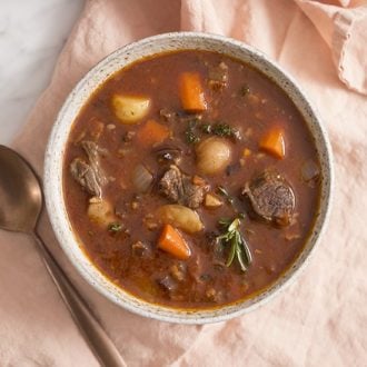 A photo of a bowl of beef stew on a pink linen napkin