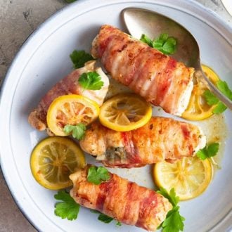 A top-down photo showing bacon wrapped chicken arranged on a white plate with lemon slices.