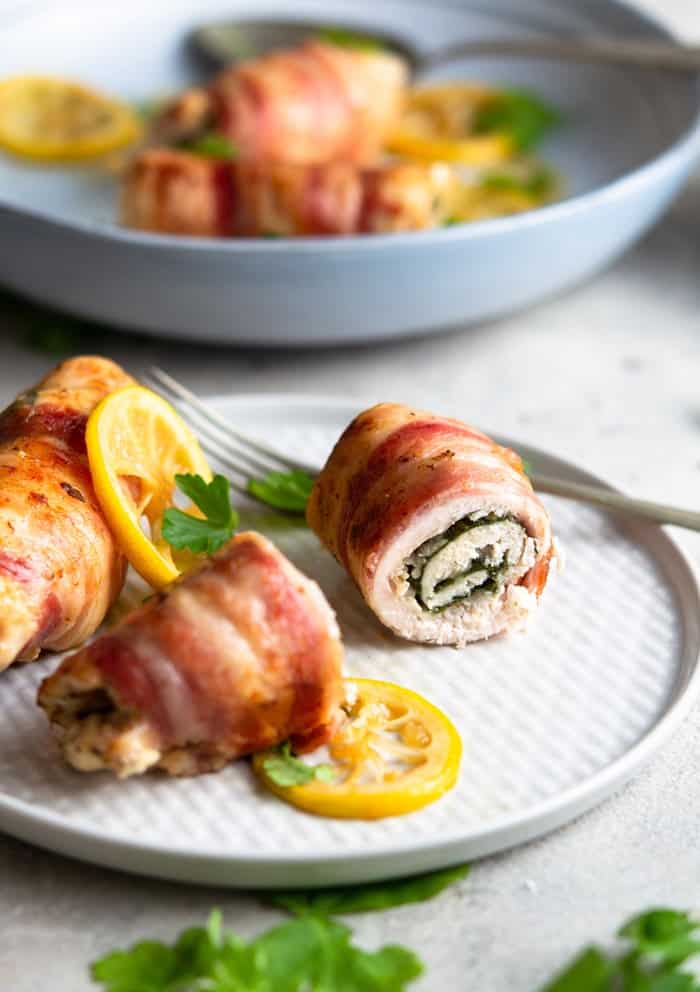 A photo showing bacon-wrapped chicken stuffed with spinach on a white plate