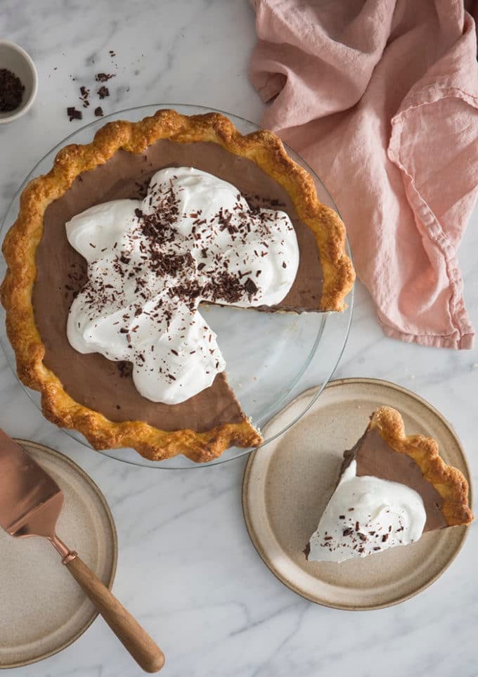 A top down photo of a chocolate pie covered in whipped cream and shaved chocolate.