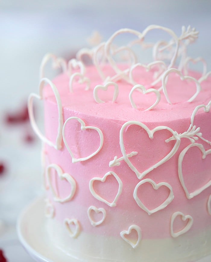 A close up photo of a pink ombré cake covered in white hearts made out of candy melts.