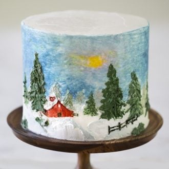 A photo showing a cake painted of a winter scene with a snow covered barn