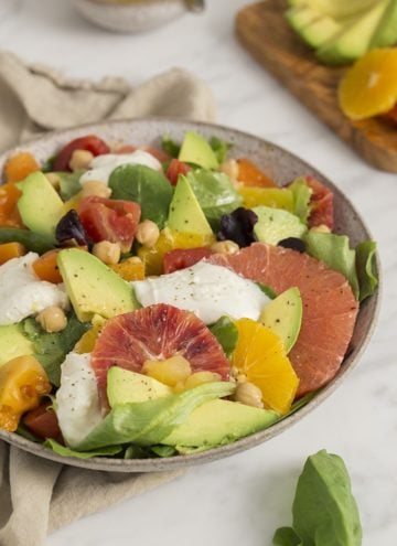 A photo of an avocado salad with various citrus premiums and burrata in a white bowl