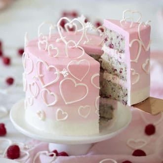 A pink ombré cake covered in white candy melt hearts.