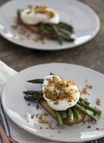 A photo of two plates on a wooden table with poached eggs on asparagus and toast.