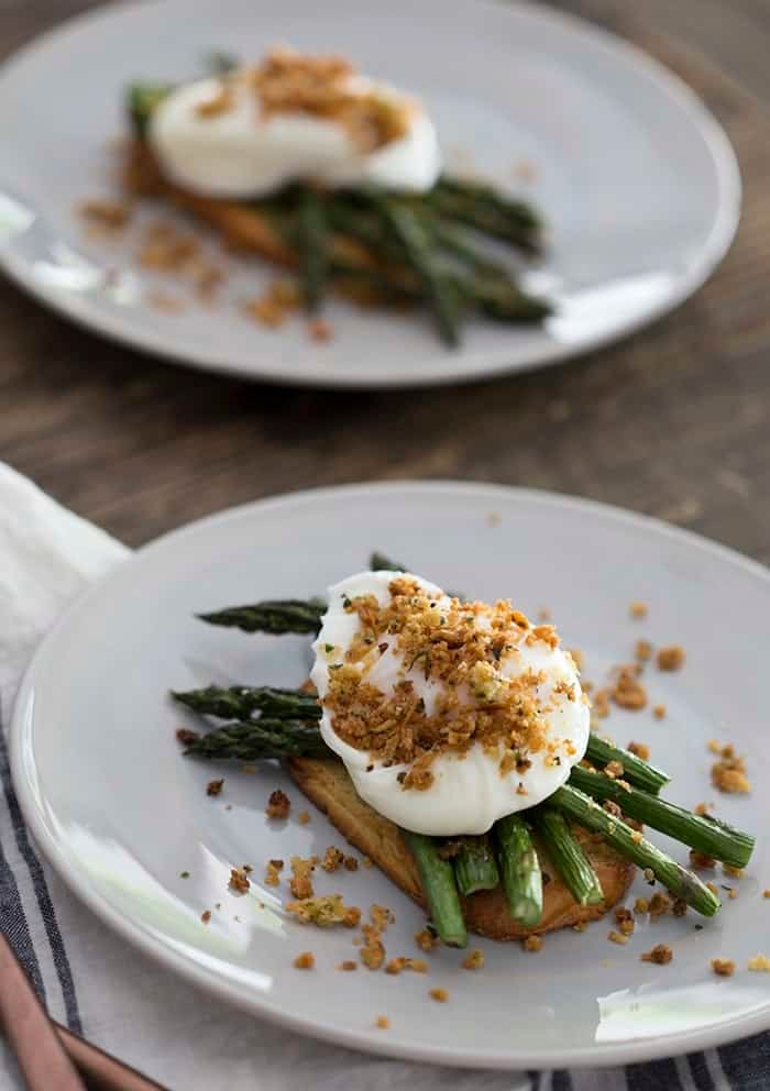 A photo of two plates on a wooden table with poached eggs on asparagus and toast.