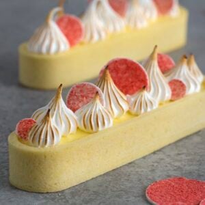 A close up image of a lemon curd tart with pink circles on top and toasted meringue dollops.