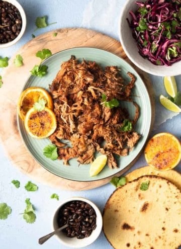 An overhead shot of slow cooker pork carnitas on a blue plate with tortillas and toppings