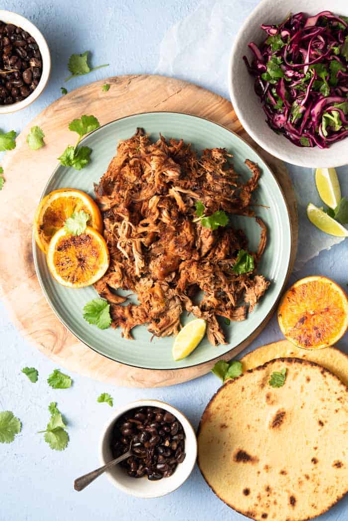 An overhead shot of slow cooker pork carnitas on a blue plate with tortillas and toppings