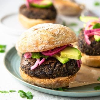A photo of a quinoa veggie burger on a plate with avocado and pickled onion.
