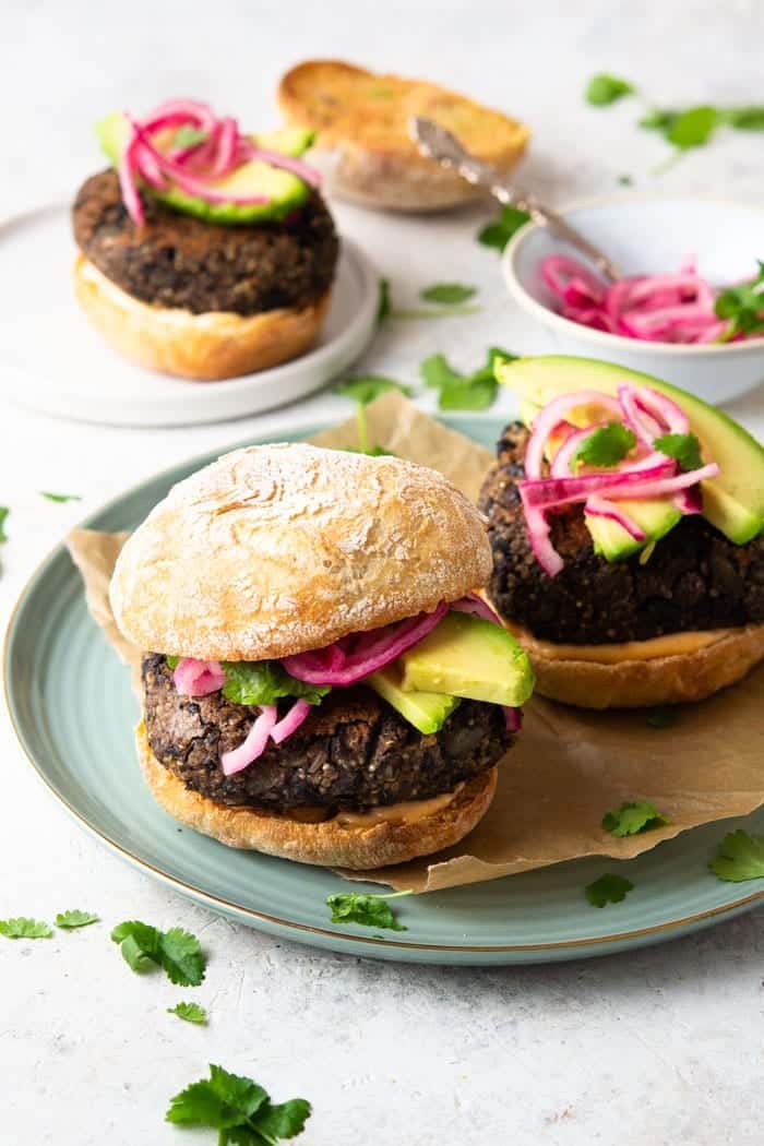 A photo of a quinoa veggie burger on a plate with pickled onions, and avocado.