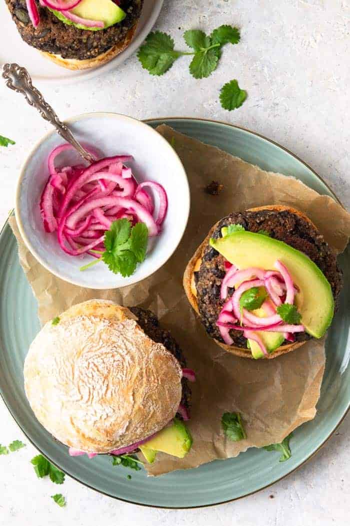 A top down shot of a veggie burger on a plate with avocado and pickled red onion.