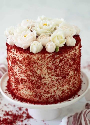A red velvet cake covered in red crumbs and topped with buttercream roses.