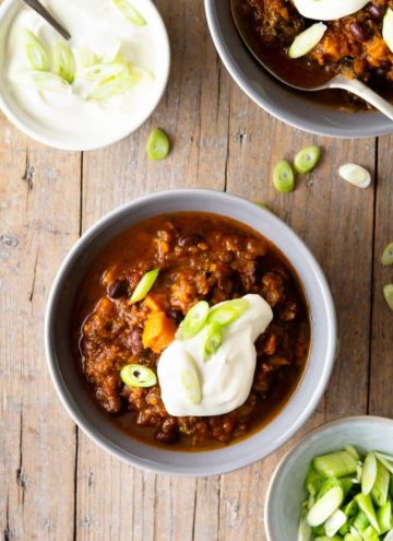 An overhead shot of a slow cooker chili in two bowls topped with sour cream and scallions