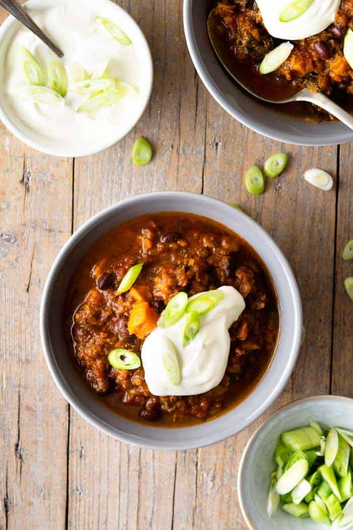 An overhead shot of a slow cooker chili in two bowls topped with sour cream and scallions