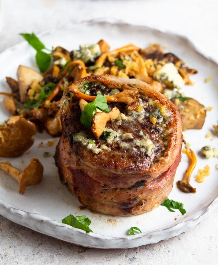 A photo showing a filet mignon with bluecheese crumbled on top and a piece of bacon wrapped around it.