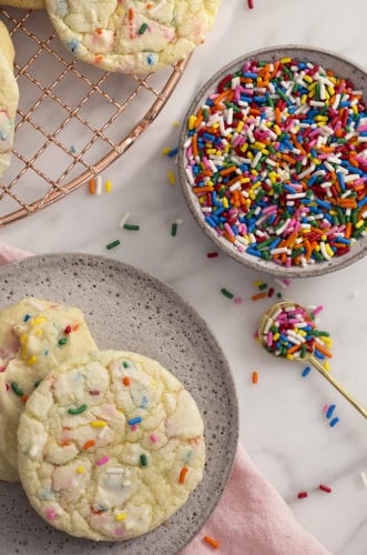 A photo showing cake mix cookies on a marble table with a bowl of sprinkles