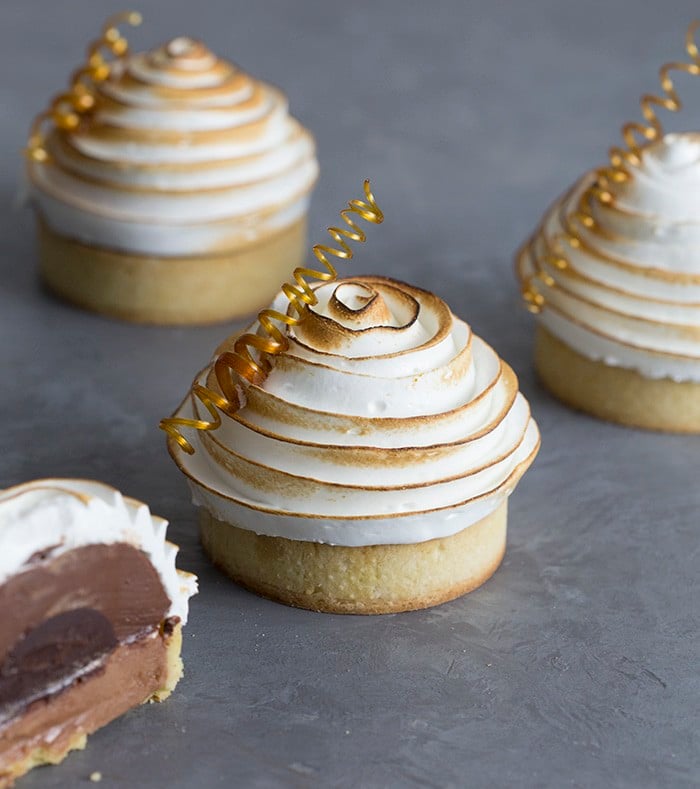 A photo showing a group of chocolate tarts on a grey surface. one has been cut in half to show the chocolate interior.