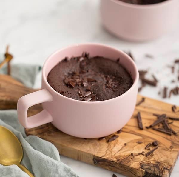 A light pink mug with a chocolate cake baked inside topped with melted chocolate.