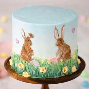 An easter bunny cake on a cake stand featuring hand painted bunnies