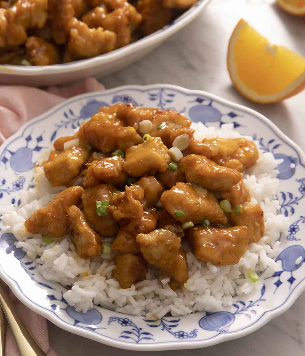 A plate of rice topped with orange chicken topped with green onions