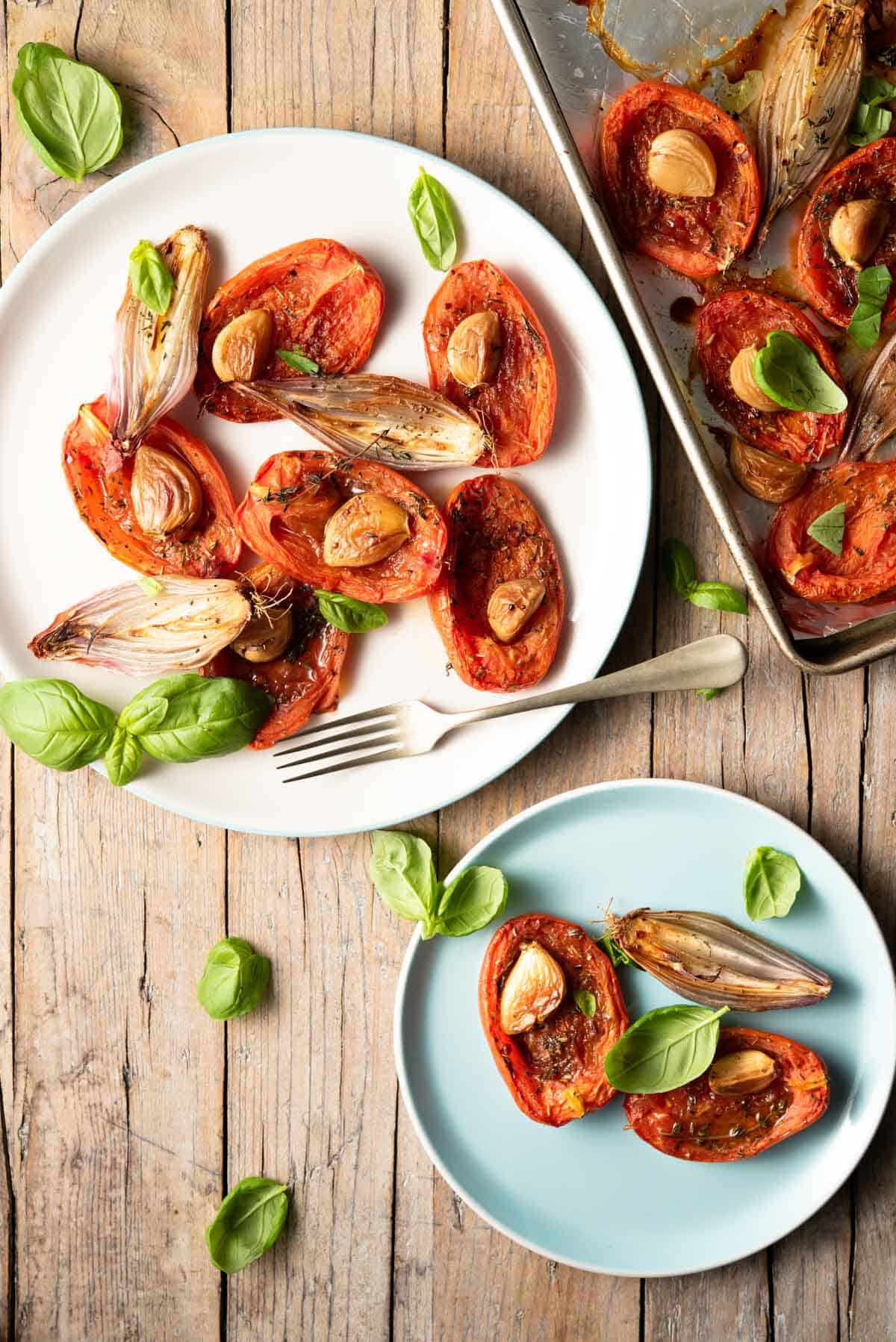 Roasted tomatoes on two serving plates with basil
