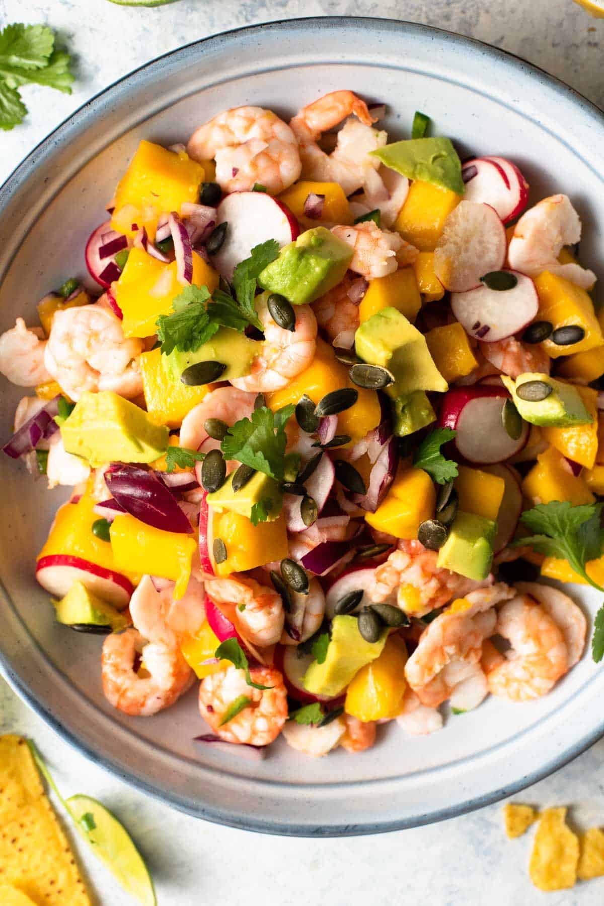 A close up of shrimp, avocado and mango in a bowl with other veggies