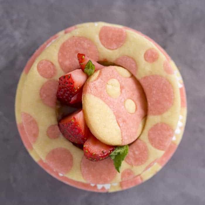 A top-down photo of a pink and white strawberry tart with fresh strawberries and a two-tone shell
