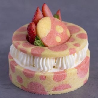 A photo of a strawberry tart with pink dots on the pastry and a strawberry on top.