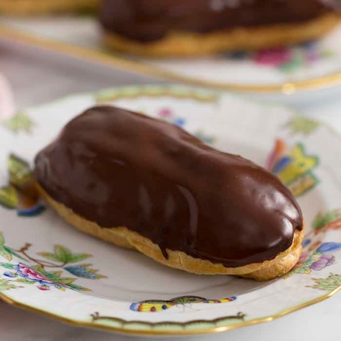 A close up photo of a chocolate eclair on a hand painted plate 
