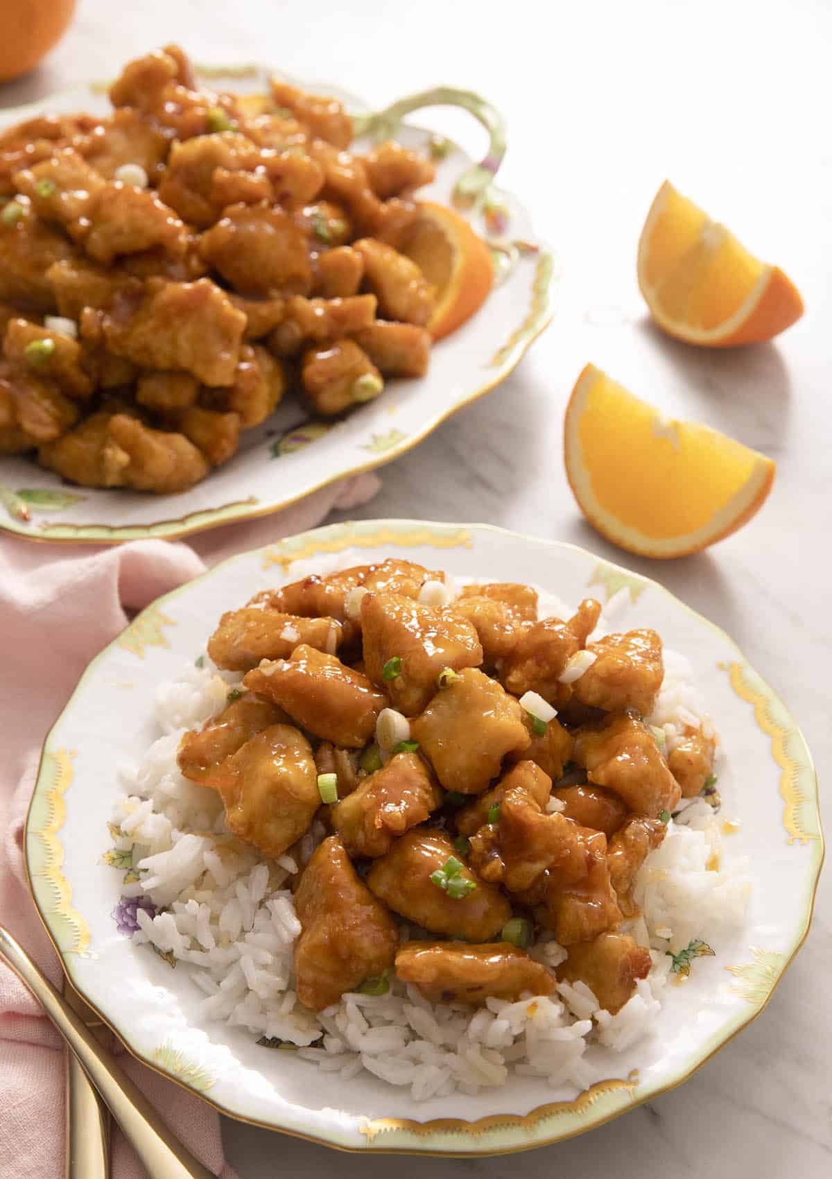 Rice and orange chicken on a plate with orange wedges in the background