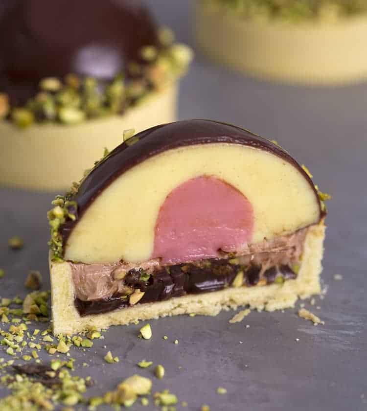 A pistachio tart cut in half showing a strawberry custard interior.