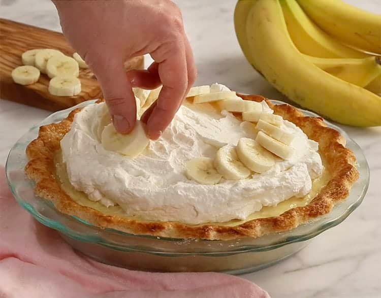 banana slices being places on a whipped cream covered pie