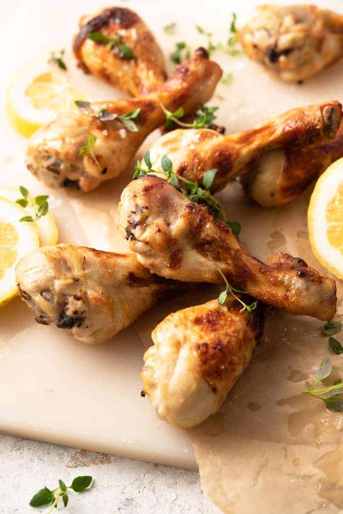 A close up of baked chicken legs on a marble board with fresh thyme and lemon