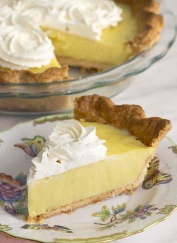 A piece of vanilla cream pie on a place next to the nearly whole pie