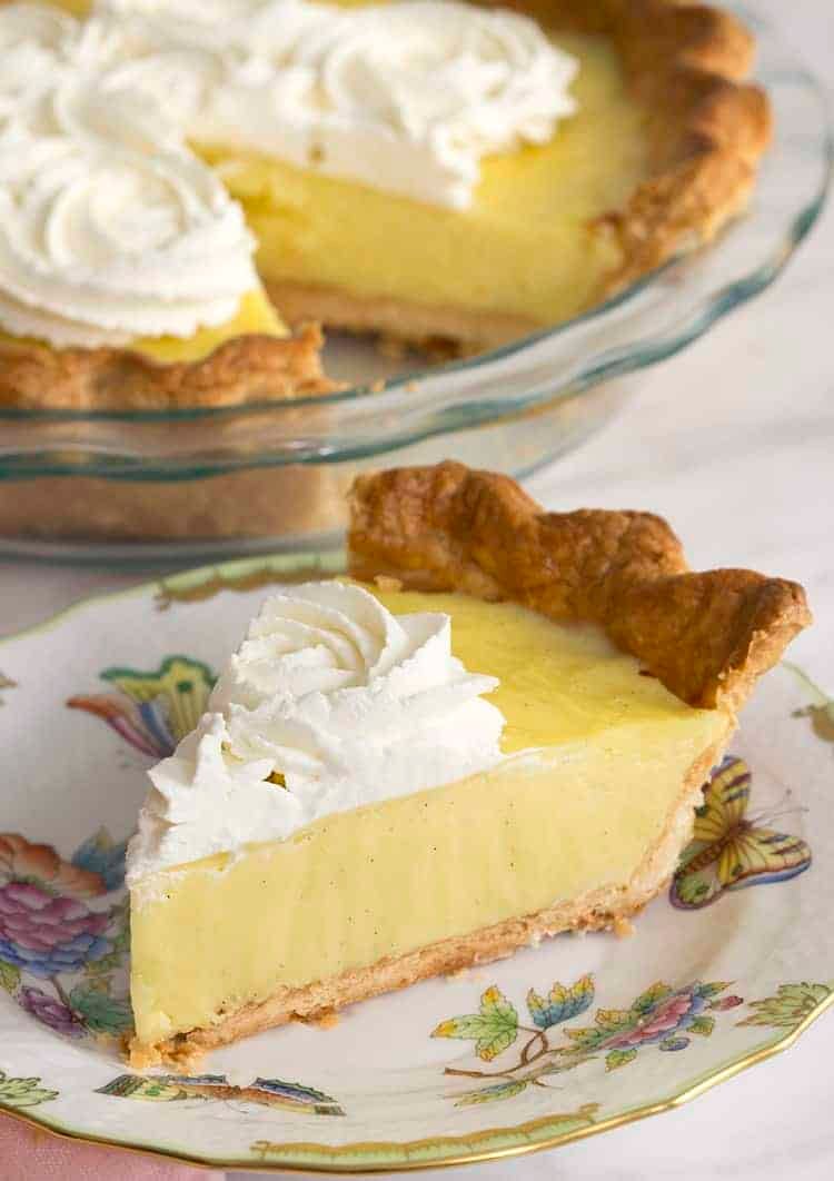 A piece of vanilla cream pie on a place next to the nearly whole pie