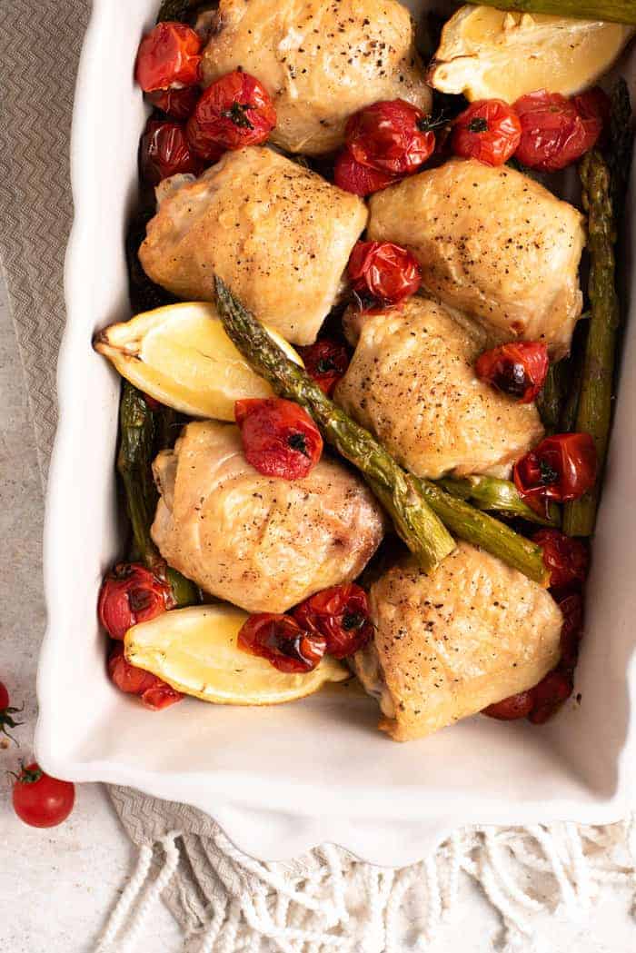 An overhead shot of roasted chicken thighs in a with asparagus and tomatoes