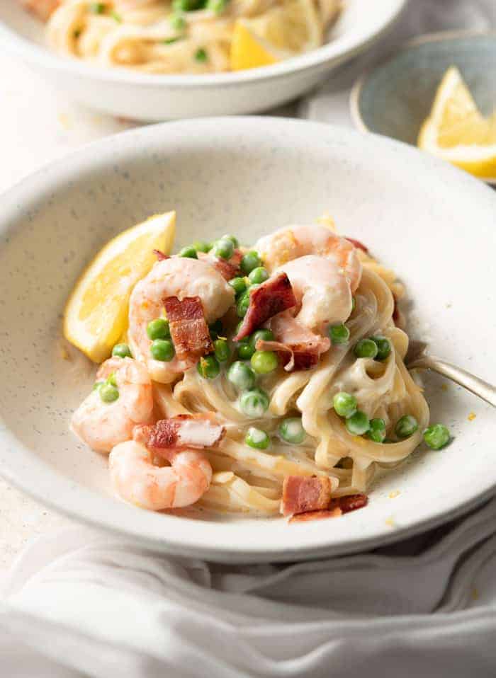 A close up of a bowl of shrimp alfredo with bacon and peas